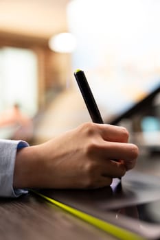 Hand of an individual holding stylus pen and sketching on illustration tablet, modifying business logo designs for companies. Closeup of a person drawing on a digital pad refining graphics on images.