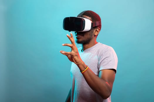 Black man exploring virtual reality, using goggles to interact with futuristic elements. Enthusiastic male gamer wearing VR headset, enjoying immersive technology, fully engaged in a digital world.