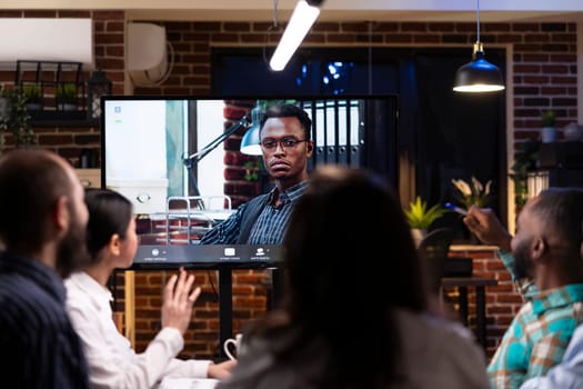 Professional black man seen on digital monitor during video call with colleagues. Male entrepreneur collaborates remotely with diverse team, discussing marketing strategy and project deadlines.