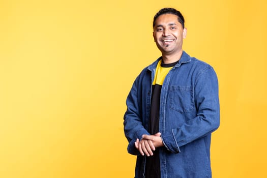 Portrait of jolly indian man smiling and posing with arms crossed standing against studio background. Joyous upbeat male person in casual clothing showcases positive emotions.