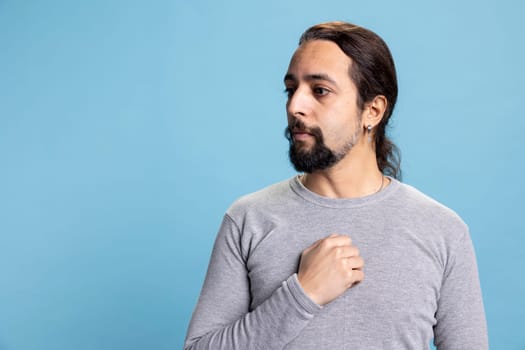 Stressed confused worried man feeling shy and insecure with anxious thoughts, overwhelmed unhappy person against blue background. Young guy with panic and fear in his eyes, desolation.