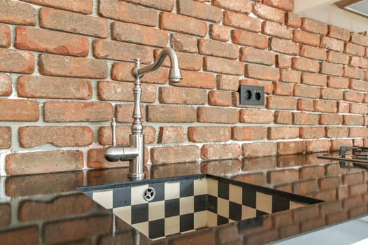 A stylish industrial kitchen featuring a rustic exposed brick wall, elegant fixtures, and a sleek countertop, combining functionality and aesthetic appeal seamlessly.