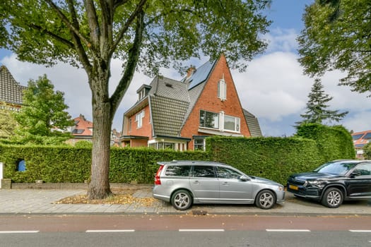 A picturesque view of a modern suburban house surrounded by lush trees and shrubs, complemented by parked cars along the street.