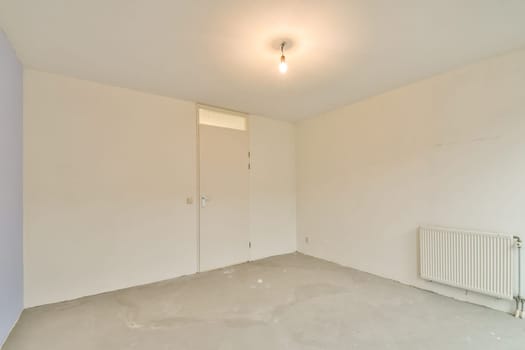 An empty room featuring a bare wall, concrete floor, and a ceiling light, creating a feeling of spaciousness and simplicity.