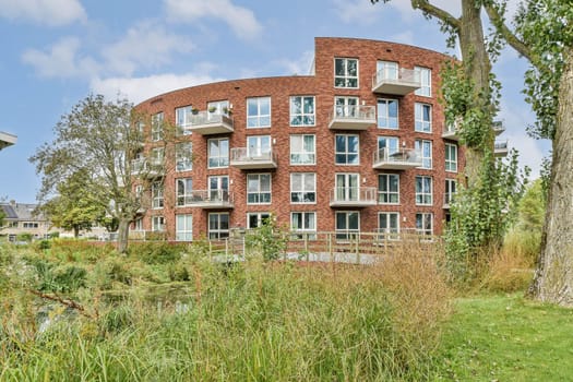 A contemporary residential building featuring large windows and balconies, harmoniously integrated with natural greenery and a serene water feature nearby.
