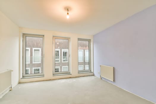 A spacious, modern interior featuring large windows that provide ample natural light. The walls are partially painted in a light color, creating a serene atmosphere.