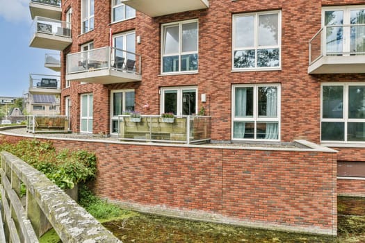 A contemporary apartment complex featuring multiple balconies, large windows, and a mix of brick and modern design elements in a lush urban setting.