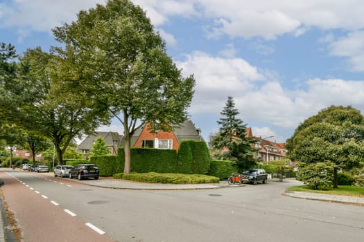 A picturesque view of a serene residential street featuring lush greenery, well-kept homes, and parked cars under a partly cloudy sky.