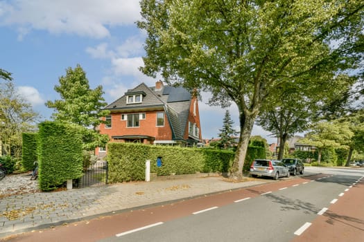 A picturesque residential street featuring a well-maintained brick home surrounded by vibrant green hedges and trees, creating a serene atmosphere.