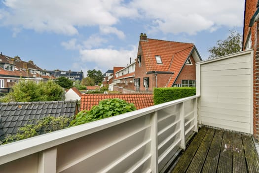 A picturesque view from a balcony, with charming rooftops and lush greenery under a blue sky. This serene scene captures tranquility in a residential area.