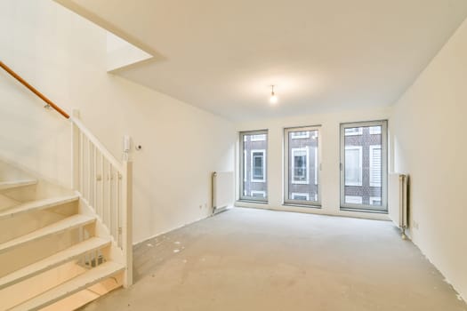 A spacious, modern interior featuring a staircase and large windows that allow natural light to illuminate the room, creating a clean and airy atmosphere.