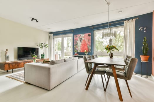 A stylish living room and dining area featuring contemporary furniture, large windows allowing natural light, and decorative plants for an inviting atmosphere.