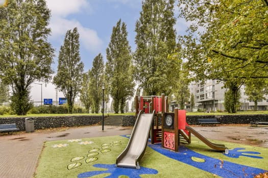 A vibrant playground featuring a red slide, surrounded by lush trees and artistic ground designs, creating a lively outdoor space for children to play.