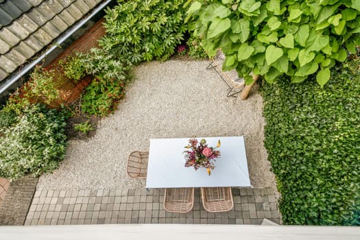 A serene garden space featuring a table adorned with flowers, surrounded by lush greenery and decorative gravel paths, perfect for relaxation or gatherings.