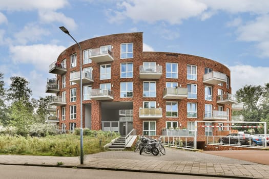 A contemporary building features unique balconies and large windows, surrounded by lush greenery, showcasing modern living harmoniously integrated with nature.