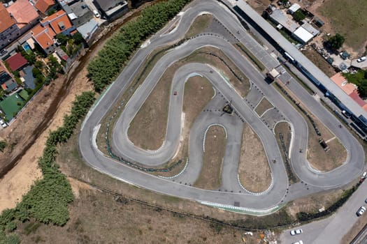 Aerial view of go-karts racing on winding tracks in countryside, capturing the excitement of a competition with cars zooming along the road from above