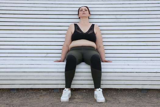 A plump,overweight, cellulite, woman over 40 in sportswear is resting on a bench after a workout.