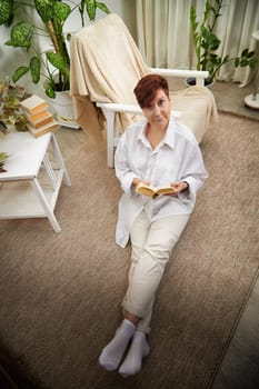 Middle-aged woman relaxes in her cozy living space while reading a book, embodying a calm lifestyle.