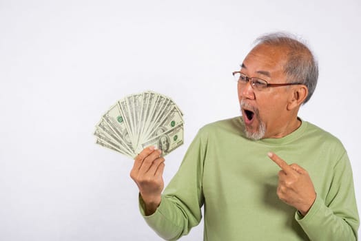 Portrait Asian smiling old man is holding a bunch of money banknotes and pointing studio shot isolated on white background. happy elderly positive excited hold dollar banknotes fan, Financial success