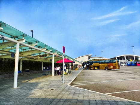 Macau, China - April 10, 2024: People wait at a bus stop in Macau, enjoying the blue sky and modern surroundings while anticipating their ride.