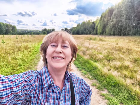 A blonde traveler blogger takes a cheerful selfie in a lush landscape during her outdoor adventure in nature.