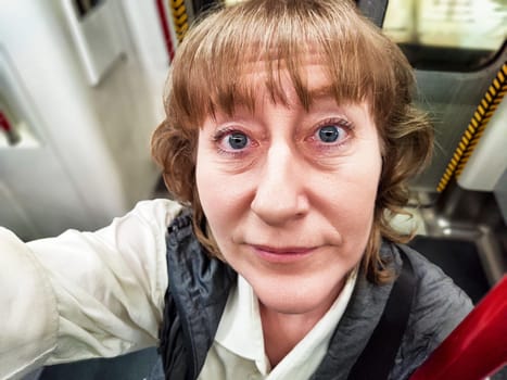 A middle-aged woman with blonde hair captures a selfie while riding the subway, enjoying her urban exploration and travel experience.