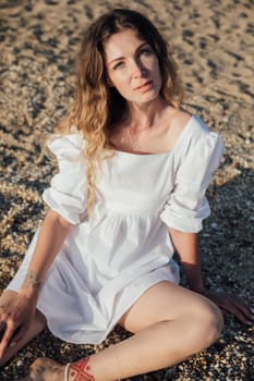 Portrait of a beautiful woman in a light summer dress on a walk on the beach by the sea