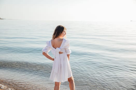 Portrait of a beautiful woman smiling in a light summer dress on the beach by the sea