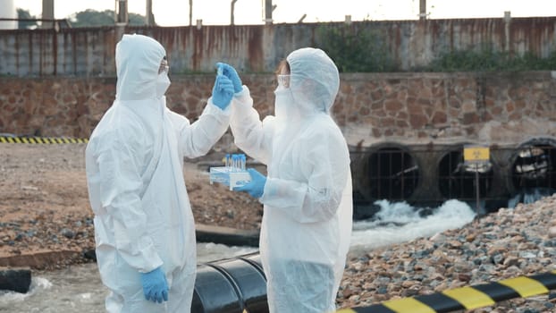 Ecologist sampling water from the river with test tube, Scientist or Biologist in a protective suit and protect mask collects sample of waste water from industrial for analyze, problem environment
