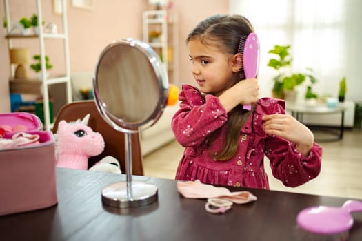 In a bright and inviting room, a young girl brushes her hair with a focused expression, surrounded by soft toys and vibrant decor. Her joyful moment reflects a playful spirit of childhood.