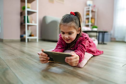 A young girl relaxes on the floor of her warm living room, absorbed in a smartphone game. Her playful spirit shines through as she enjoys this quiet activity in a comfortable, stylish space.