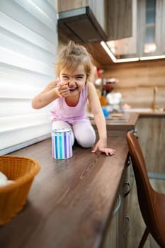 A young child joyfully indulges in a playful snack experience, sitting on the kitchen counter with a can of colorful treats, reflecting pure delight and curiosity in a warm environment.