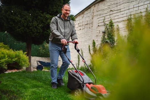 A cheerful man is mowing his lush green lawn, surrounded by vibrant plants and bushes in a well-kept garden. The sky is clear, suggesting a pleasant afternoon in suburbia.