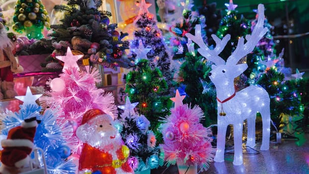 Luminous reindeer and santa claus figurines illuminating colorful christmas trees