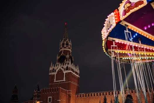Brightly lit carousel in front of the majestic Moscow Kremlin at night, creating a magical festive atmosphere