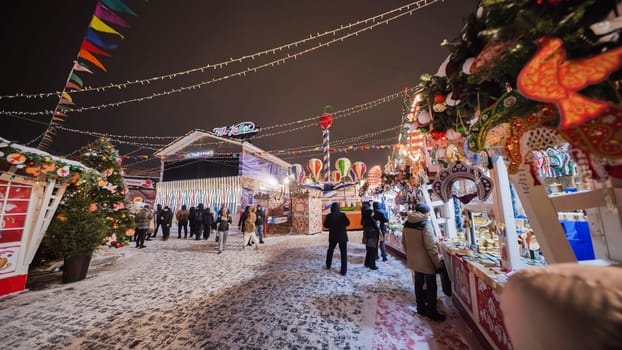 Tourists enjoying snowy Christmas market with traditional russian gifts, decorations, food and attractions in Moscow, Russia