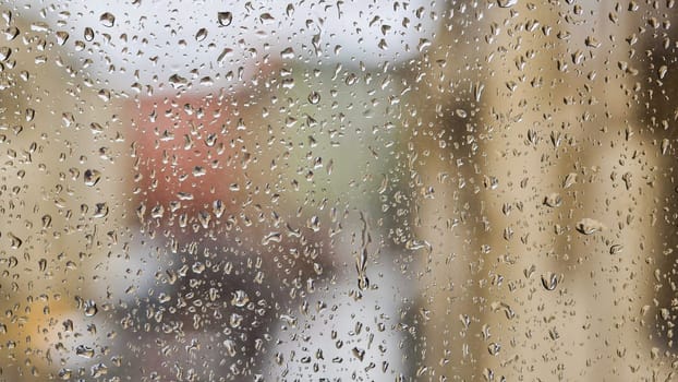 Transparent raindrops sliding on window glass during rainy day blurring city buildings in background, creating abstract pattern