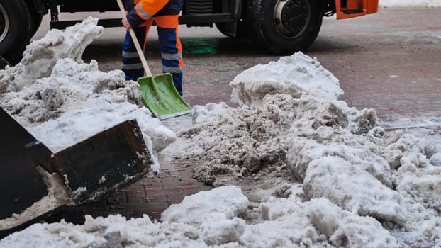 Road worker cleaning snow from street with shovel and truck in winter