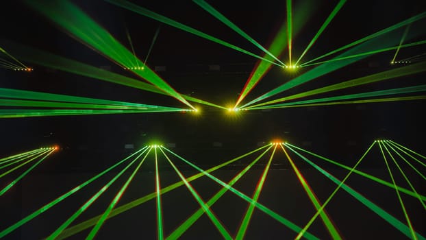 Green laser lights are crossing the darkness of a concert hall during a music festival
