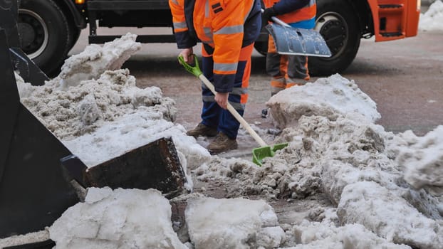 Tractor shovel loading snow and ice into truck during winter road cleaning.