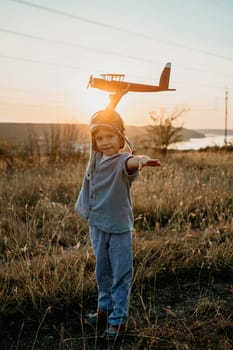 Portrait of funny little boy in aviator helmet ready to fly as airplane on nature background. Kids dream is to be pilot. Fun, creative dream, fantasy