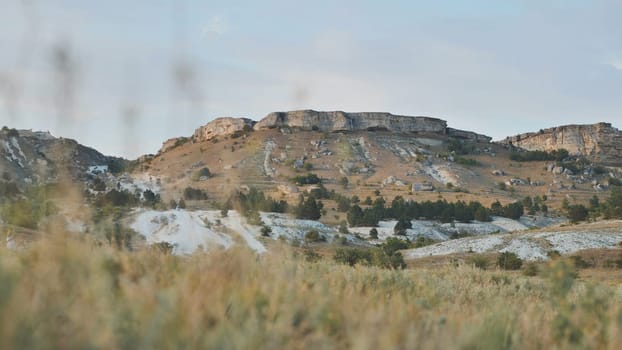 Scenic view of White Rock mountain in Crimea, near Belogorsk, featuring dry grassland, coniferous trees, and a rocky terrain under a clear sky