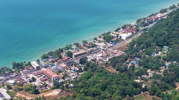 Aerial perspective captures a vibrant coastal town bordered by turquoise waters and dense green forests, showcasing a harmonious blend of urban development and natural beauty