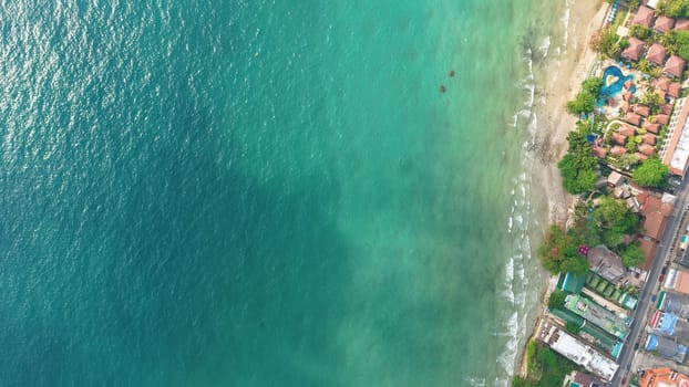 Turquoise water gently laps the sandy shore of a tropical beach resort, while a lone catamaran sails serenely nearby, capturing the essence of a tranquil island getaway