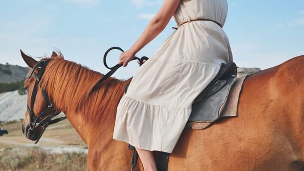 Woman wearing long white dress riding brown horse in the mountains of Crimea near the town of Belogorsk