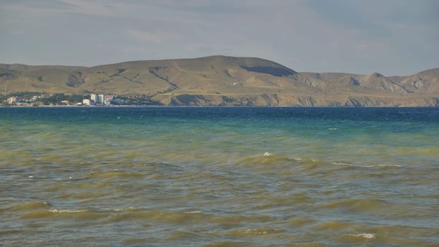 Small waves gently rolling in Koktebel bay, with mountains and buildings in the background