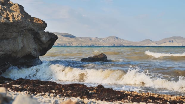Seascape with waves crashing on Crimean beach with rocks and mountains in the distance