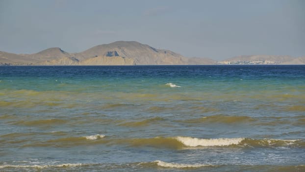 Calm sea waves washing the coast of Crimea with mountains and city in the background