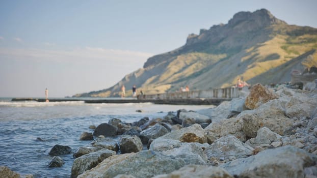 Rocky beach with blurred people strolling on a pier and mountains in the background in Crimea