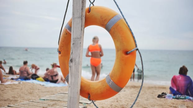 Orange lifebuoy secured on wooden pole, marking rescue point near swimmers and sunbathers along black sea coastline in crimea